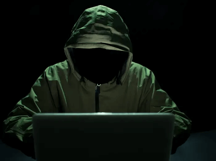 A person in green robes with their face hidden while using a laptop